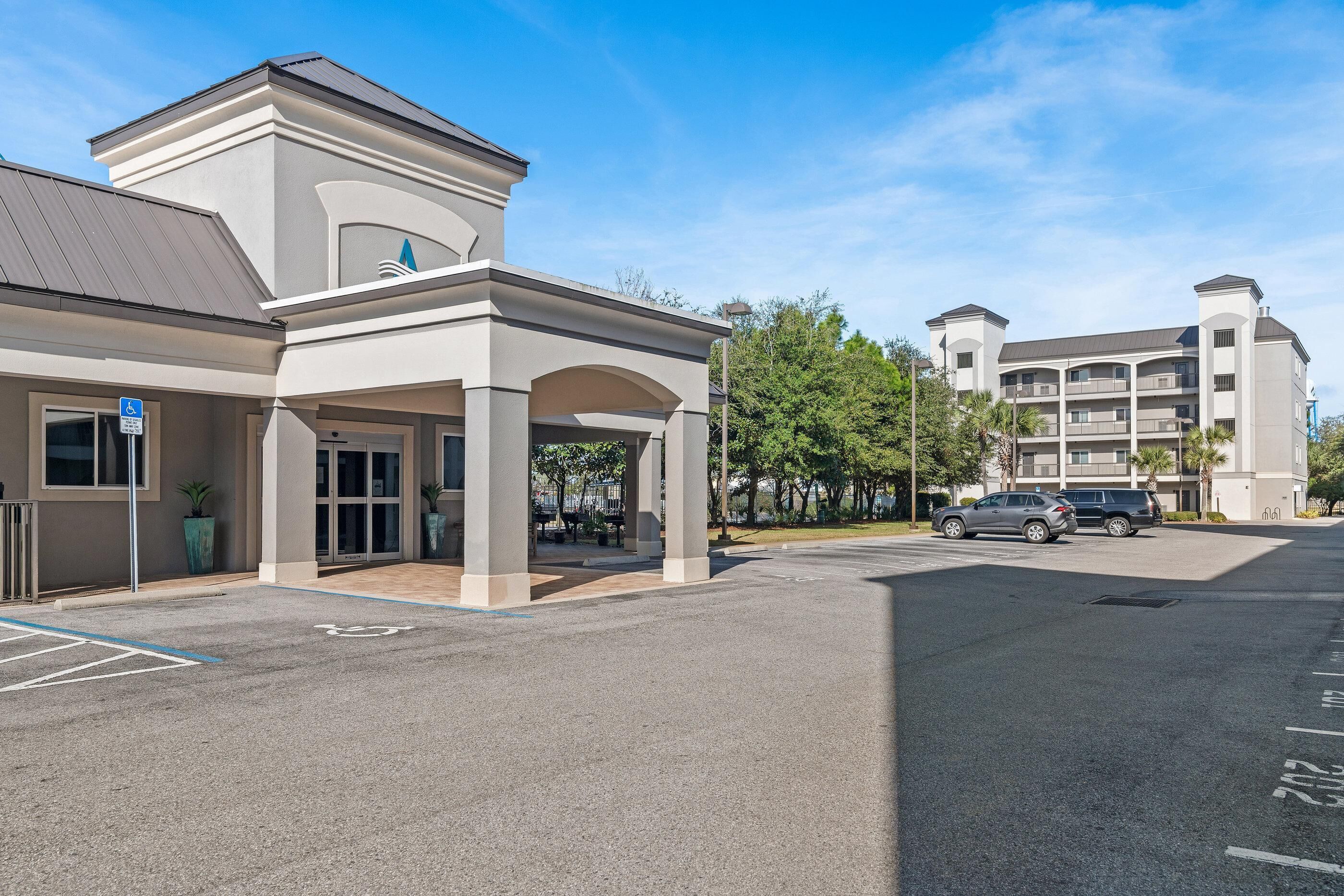 A hotel entrance with a covered walkway, a parking lot, and a multi-story building in the background.