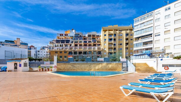 A rooftop pool area with blue lounge chairs, a small pool, and a view of multi-story buildings. - Inftour Apolo IV Apartamento (Calp)