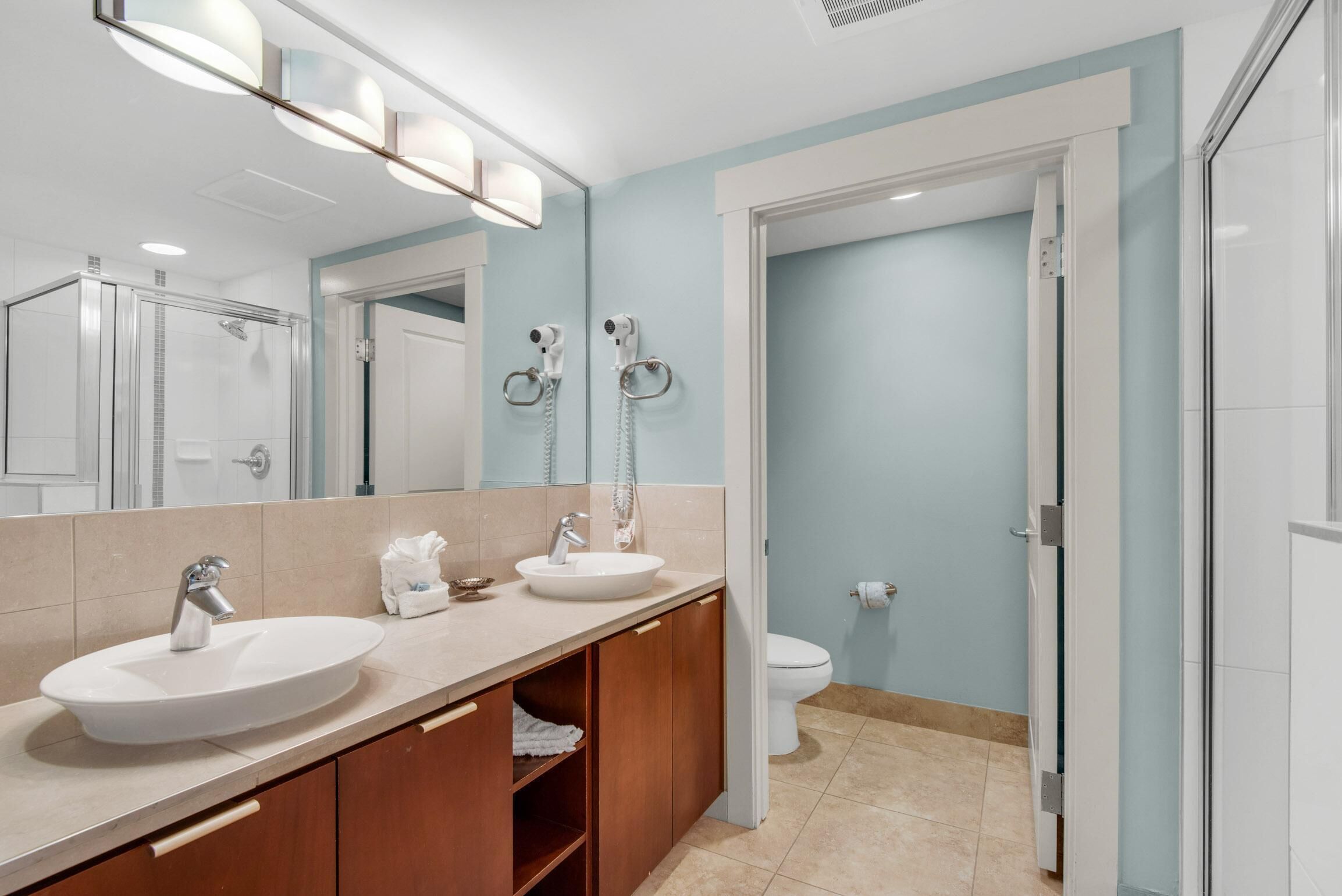 A modern bathroom with two sinks, a large mirror, and a shower enclosure.