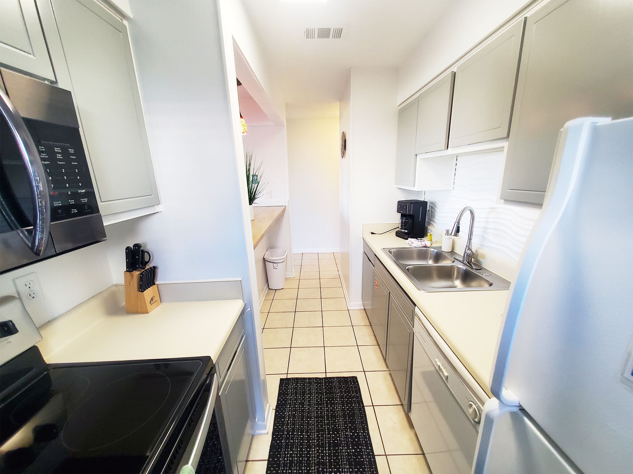 A compact kitchen with a microwave, stove, sink, and coffee maker.