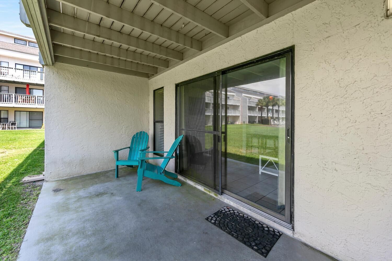 Un patio techado con puerta corrediza de vidrio, una silla Adirondack color turquesa y piso de concreto.
