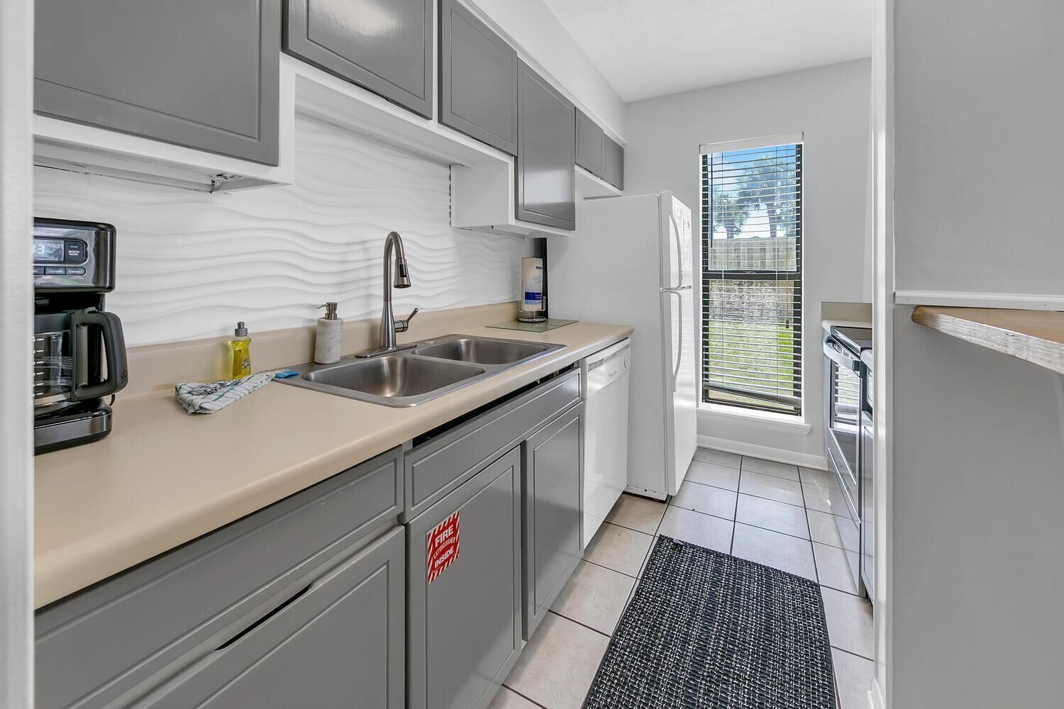 A compact kitchen with a double sink, a coffee maker, and a refrigerator.