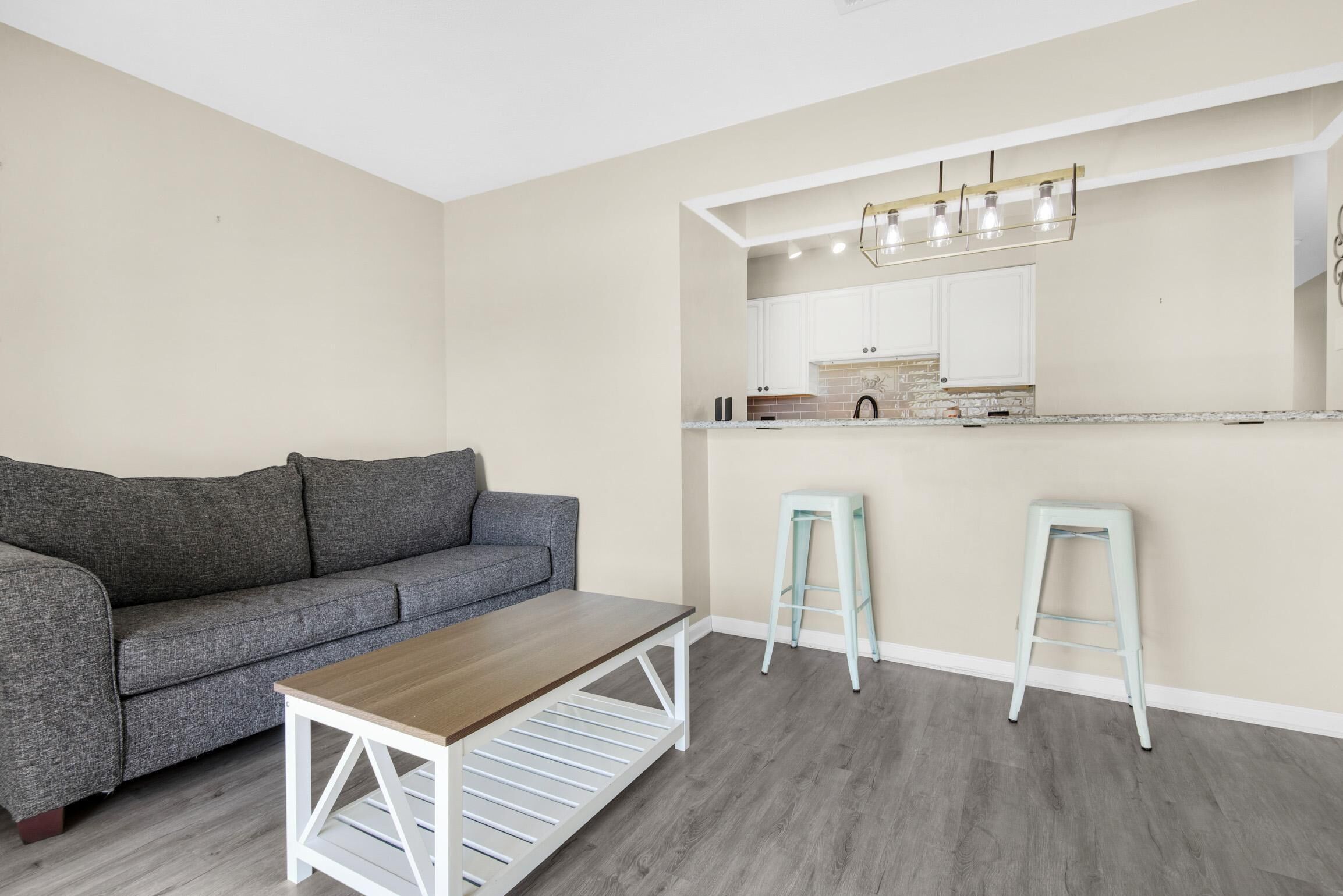 Una sala de estar con un sofá gris, una mesa de centro de madera y dos taburetes azul claro.