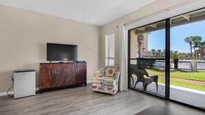 A spacious room with a large sliding glass door leading to a balcony, a wooden cabinet with a flat-screen TV, and a patterned armchair. - Endless Summer E2 (Panama City Beach)