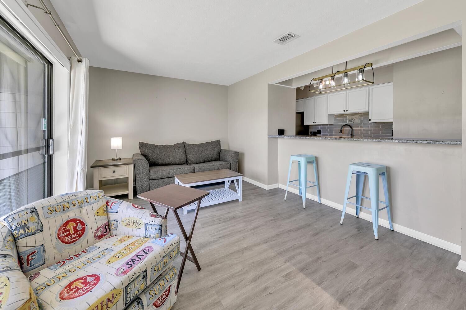 Un espacio habitable compacto con sofá, una mesita y una kitchenette con taburetes.