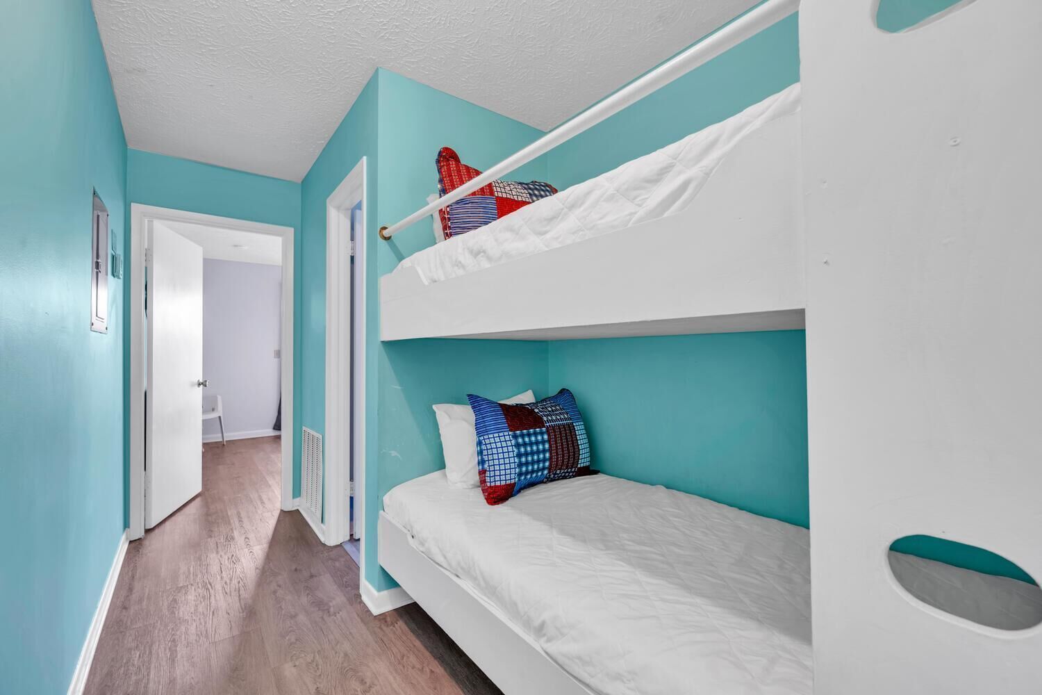 A room with two bunk beds, teal walls, and a wooden floor.