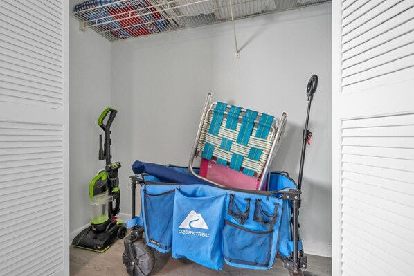 A room with a blue cleaning cart, a green vacuum cleaner, and a folded blue and white striped chair.