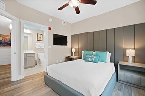 Ein Hotelzimmer mit einem großen Bett, einem Deckenventilator, einem an der Wand montierten Fernseher und einem durch eine offene Tür einsehbaren Badezimmer.