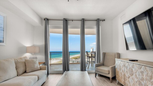 A modern hotel room with a balcony, a sofa, a coffee table, and a TV mounted on the wall. - Calypso 3-1511 (Panama City Beach)
