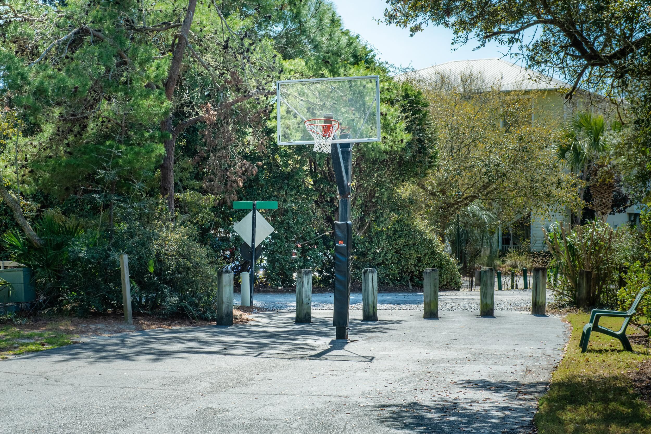 An outdoor basketball court with a hoop, surrounded by trees and a bench.