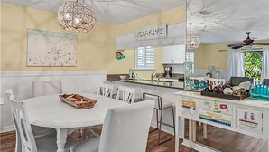 A dining area with a white table and chairs, a kitchen in the background, and a ceiling with a unique design. - Cassine Gardens 212 (Santa Rosa Beach)