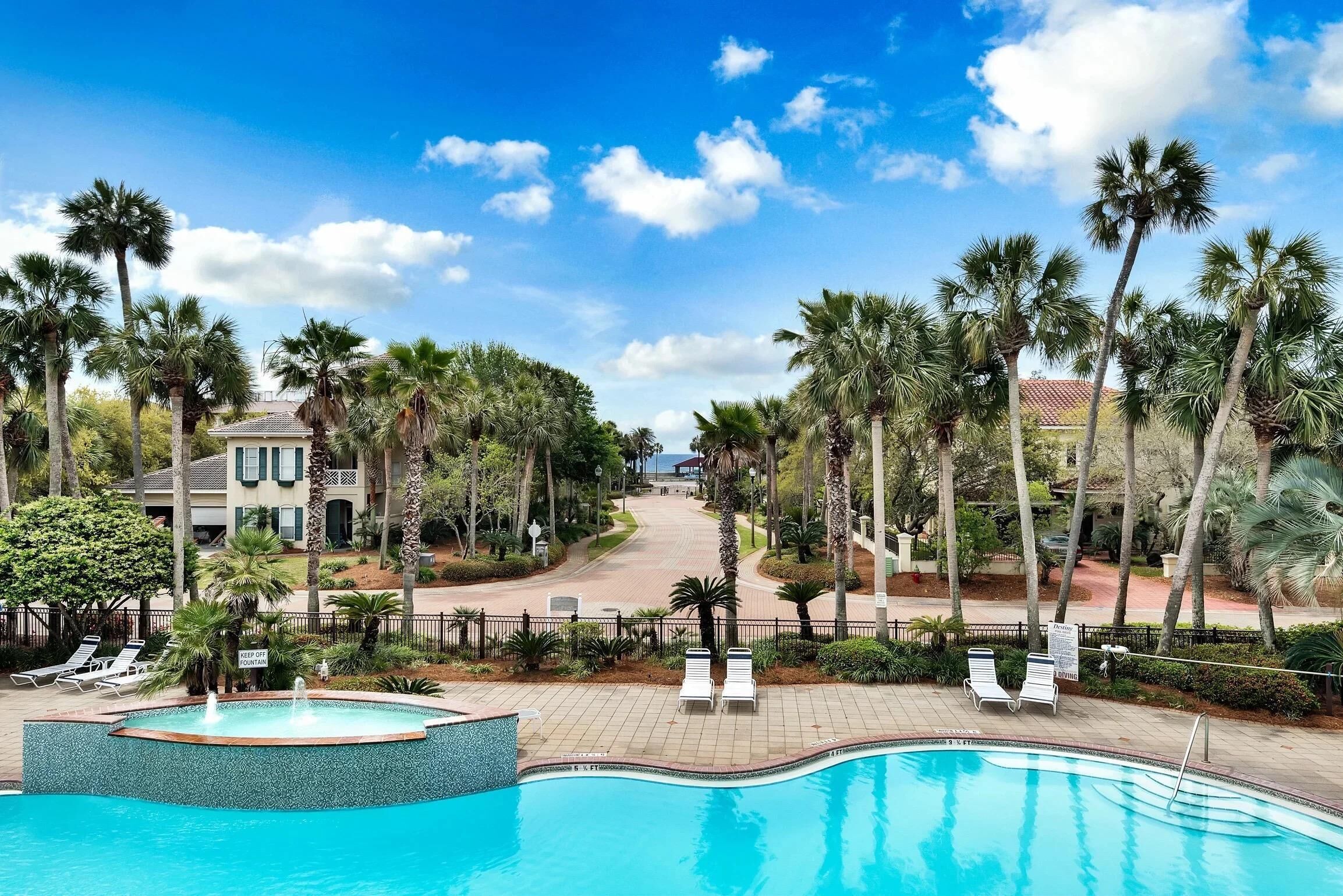 A swimming pool with lounge chairs, surrounded by palm trees and a clear sky.
