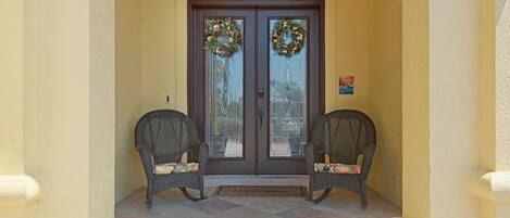 A double door with glass panels and two wicker chairs with cushions in front.
