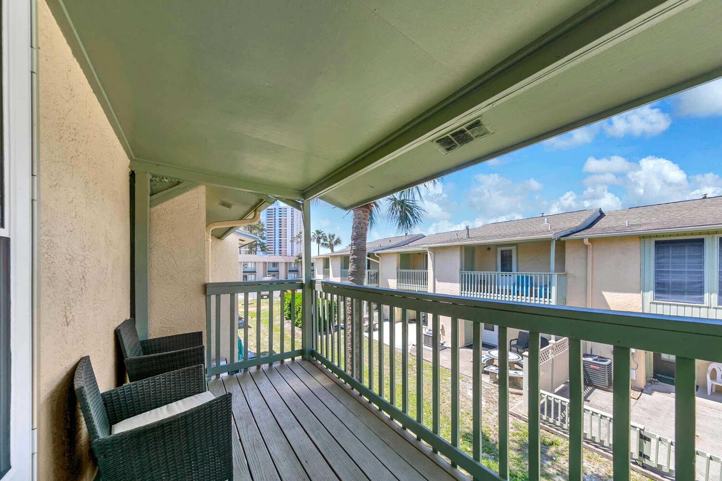 Een balkon met rieten stoelen en uitzicht op omliggende gebouwen, onder een heldere lucht.
