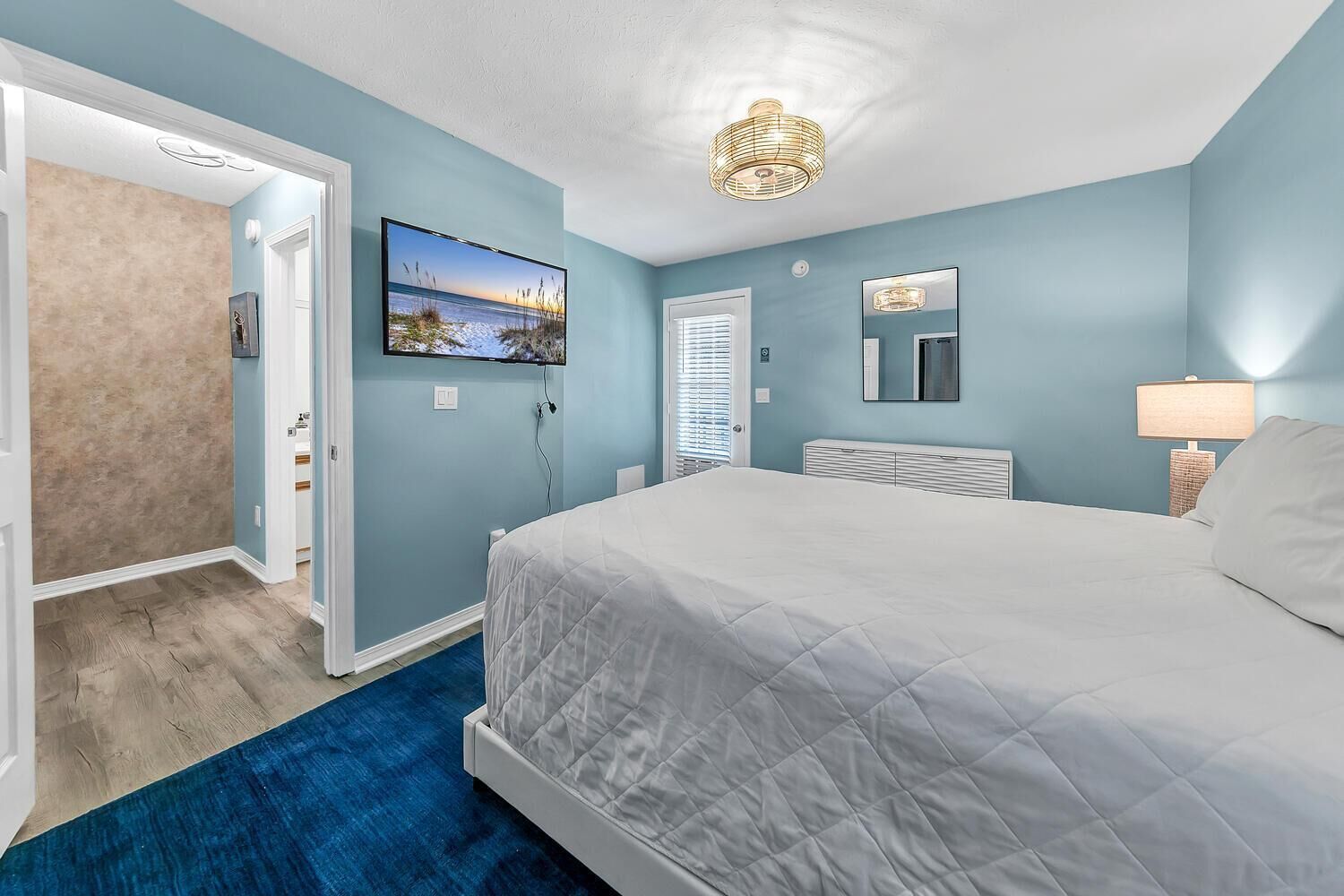 Een slaapkamer met een groot bed, een aan de muur bevestigde televisie, een raam met zonwering en een plafondlamp.