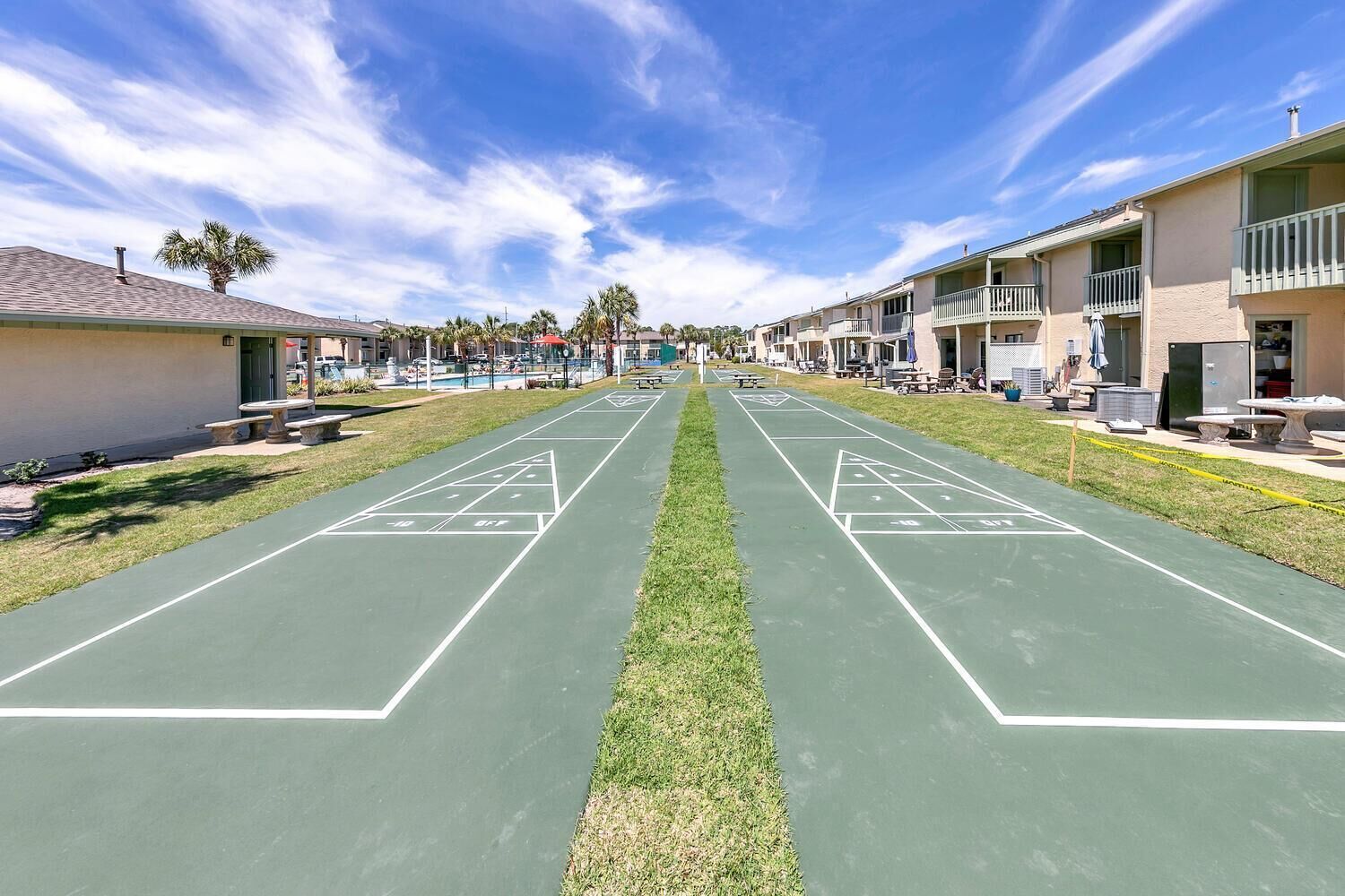 A shuffleboard court with a clear sky, surrounded by buildings with balconies and outdoor seating.