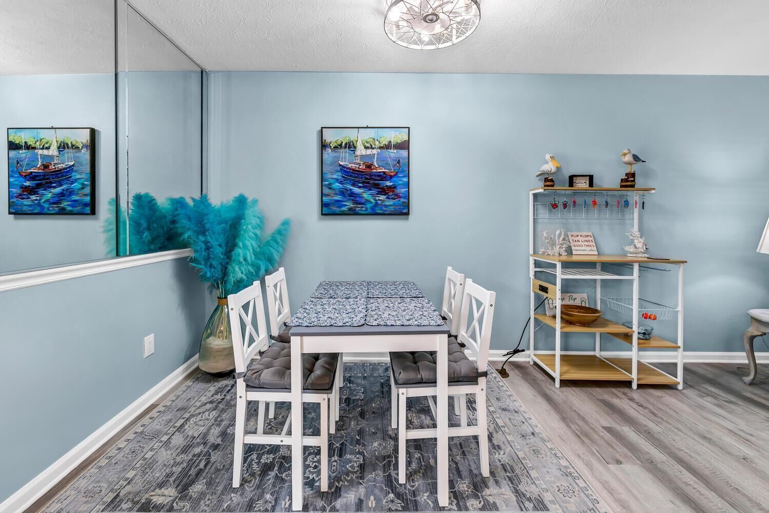 A dining area with a table and chairs, a decorative plant, and a shelf with kitchen utensils.