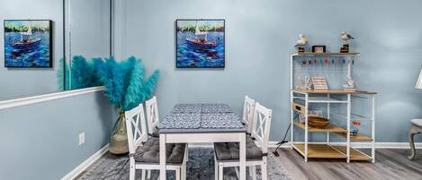 A dining area with a table and chairs, a decorative plant, and a shelf with kitchen utensils.