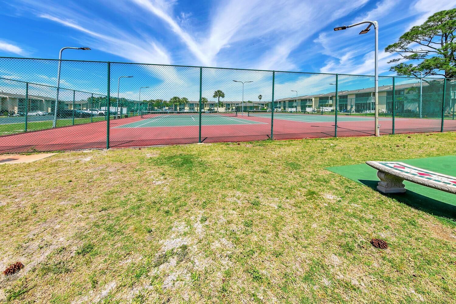 A tennis court with a green fence, a red track, and a green field area.