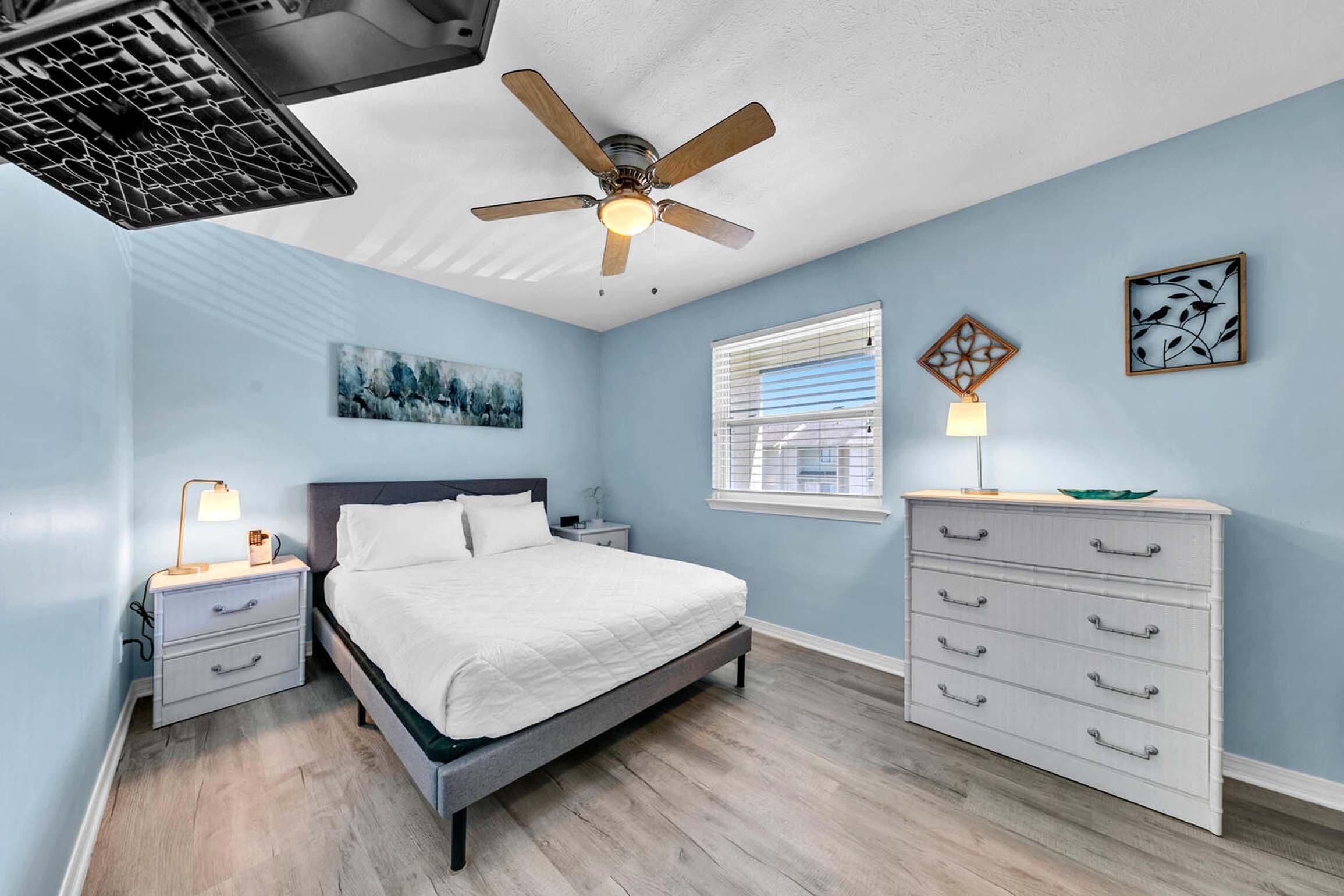 A bedroom with a bed, nightstands, a dresser, a ceiling fan, and artwork on the walls.