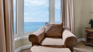 A corner room with a view of the sea, a beige armchair, and a wooden side table. - Emerald Beach 930 (Panama City Beach)
