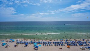 A beach with rows of blue umbrellas and sun loungers, a clear sky, and the ocean. - Emerald Beach 930 (Panama City Beach)