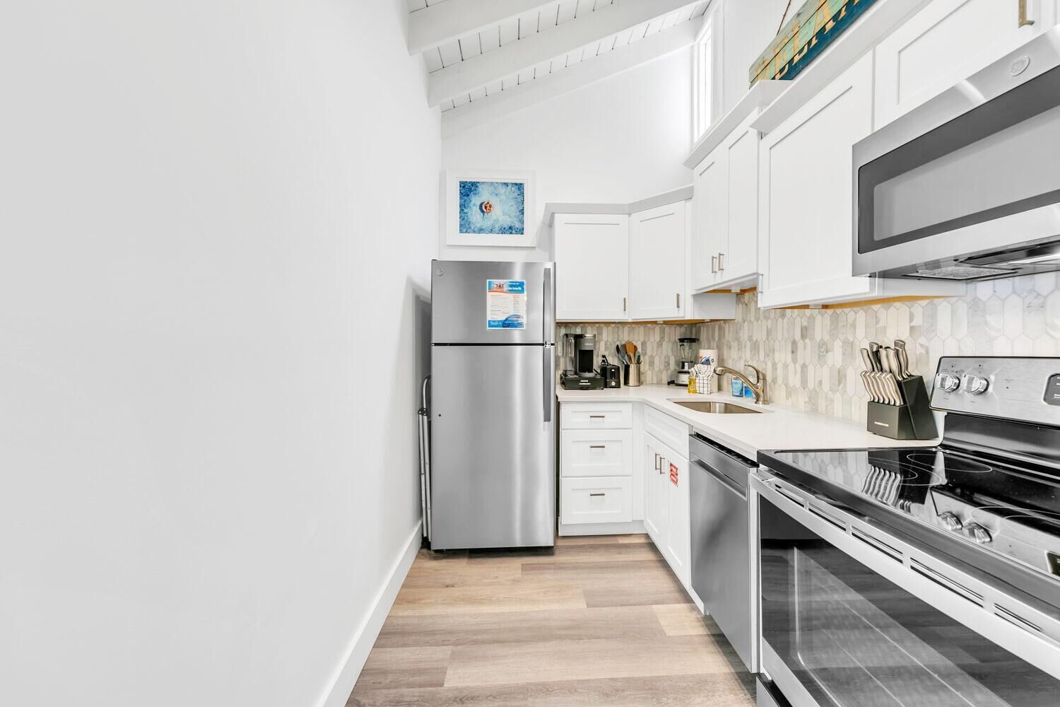 A modern kitchen with white cabinetry, stainless steel appliances, and a wooden floor.