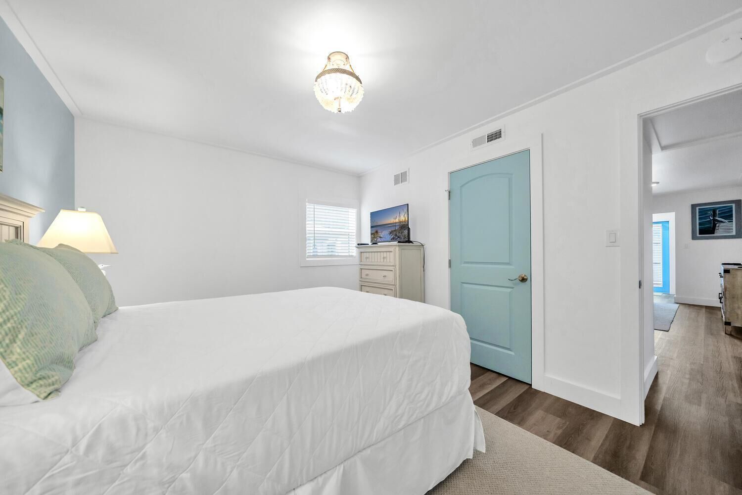 A bedroom with a large bed, a dresser, a desk, and a door leading to another room.