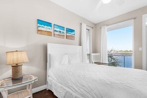 Relax in this serene bedroom with a large bed, glass table, and stunning views of a body of water.