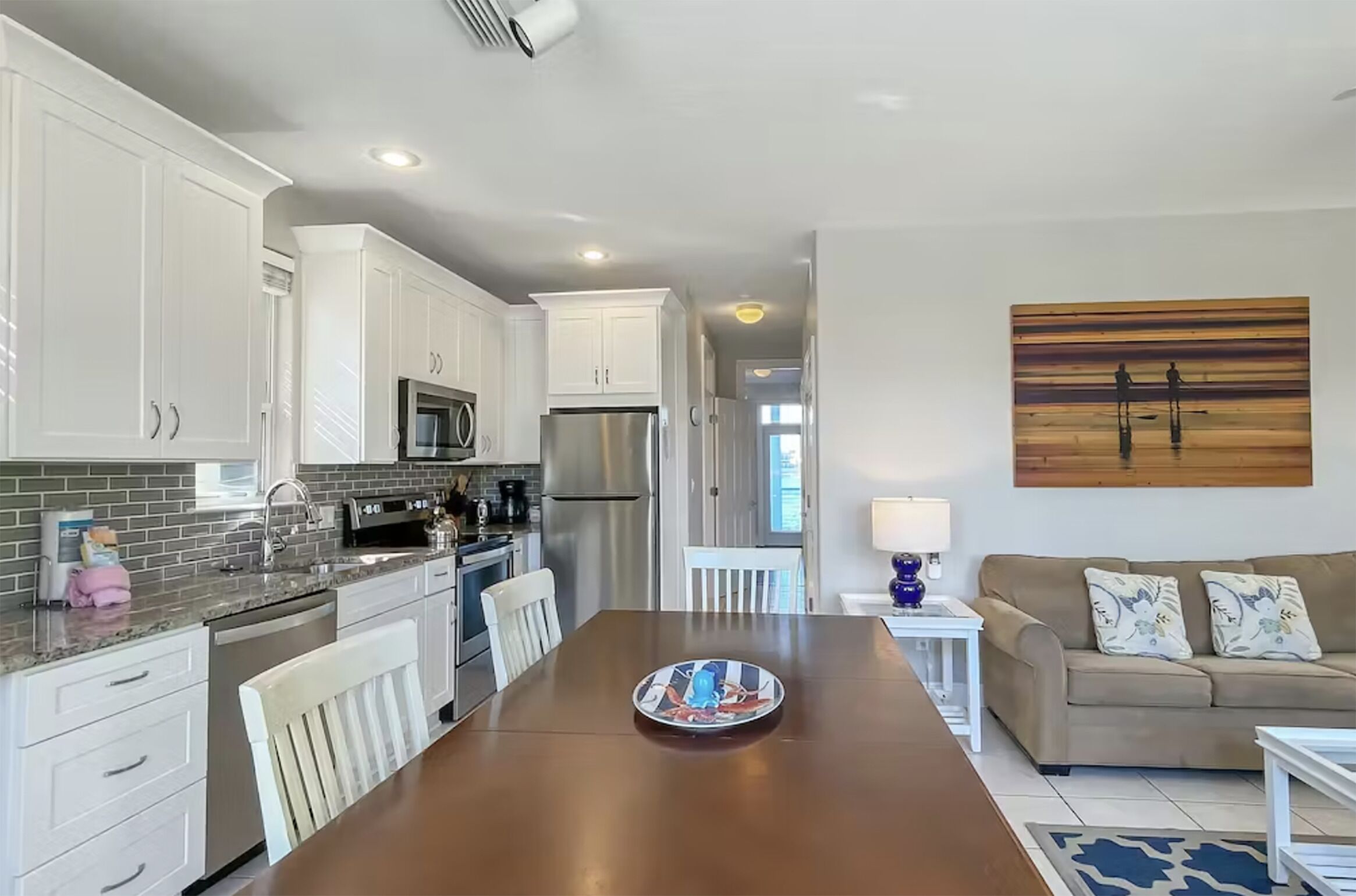 A modern kitchen with white cabinets, stainless steel appliances, and a dining area with a wooden table and white chairs.