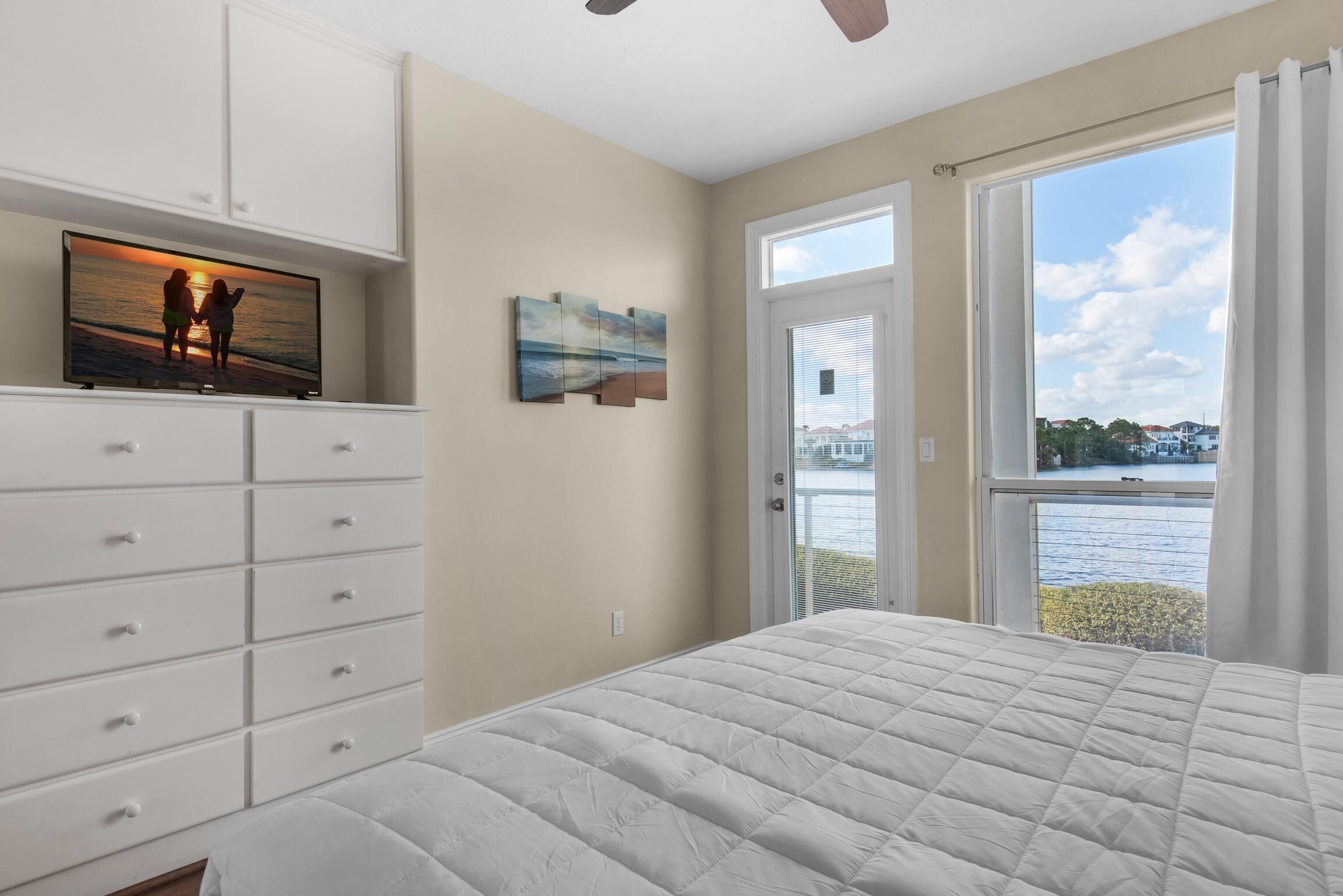 Une chambre avec un grand lit, un téléviseur posé sur une commode, une porte donnant sur un balcon et un tableau accroché au mur.