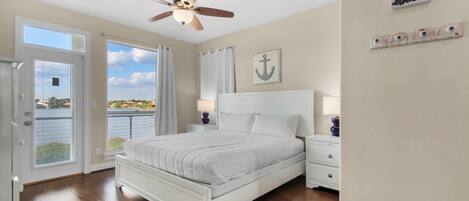 A bedroom with a bed, a ceiling fan, a view of the outdoors, and a sign on the wall.