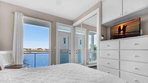 A bedroom with a large bed, a TV on a dresser, and a view of the sea through the open door. - Destiny Beach Villas #11a&b- Beach Oasis (Destin)