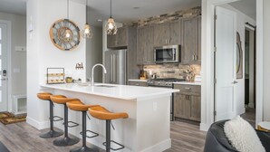 Una cocina moderna con una isla central, taburetes de bar y una lámpara colgante.