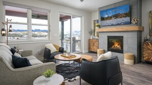 Una sala moderna con chimenea, ventanas amplias y vistas a montañas.