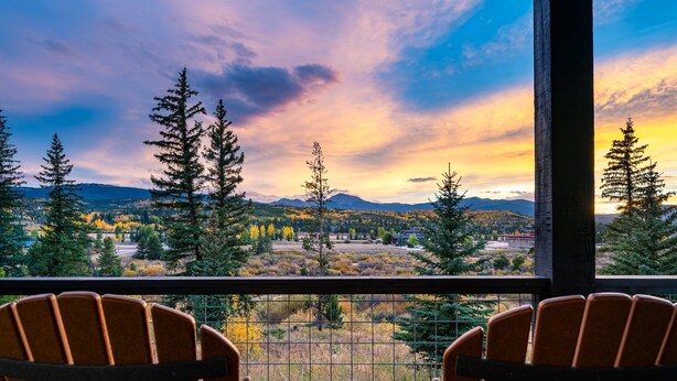 Un balcón con dos sillas de madera y una mesa, con vistas a un paisaje pintoresco de montañas y árboles.
