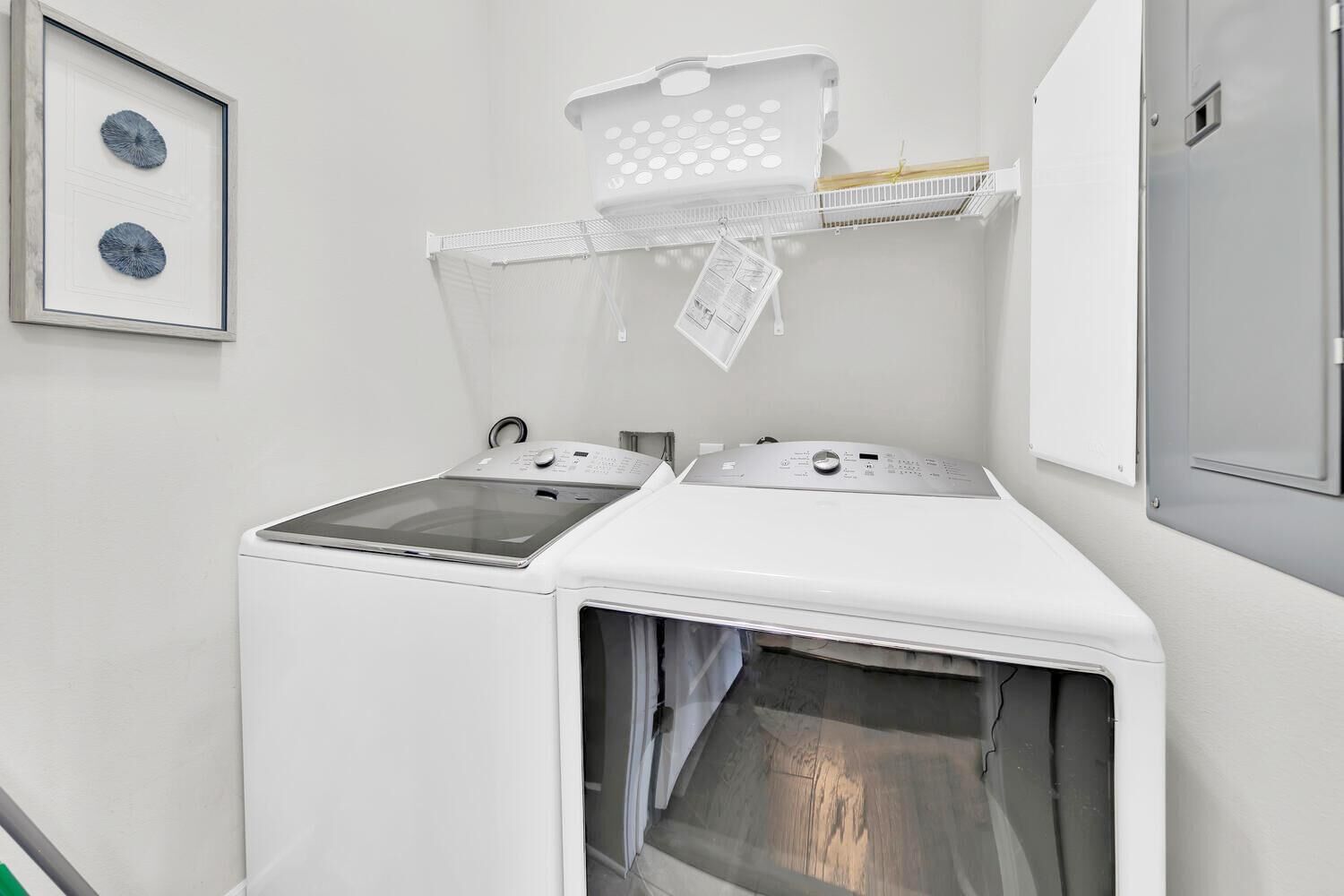 A laundry room with two washing machines and a dryer, a white wall, and a framed picture above the machines.
