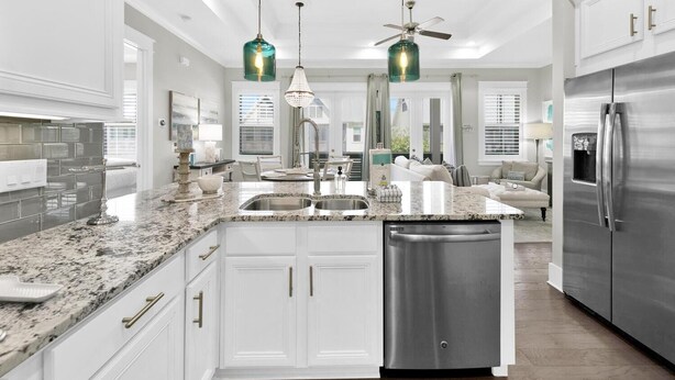 A modern kitchen with white cabinetry, a stainless steel refrigerator, and a central island with a sink. - Town of Prominence 67C - Pour Beach Life (Santa Rosa Beach)