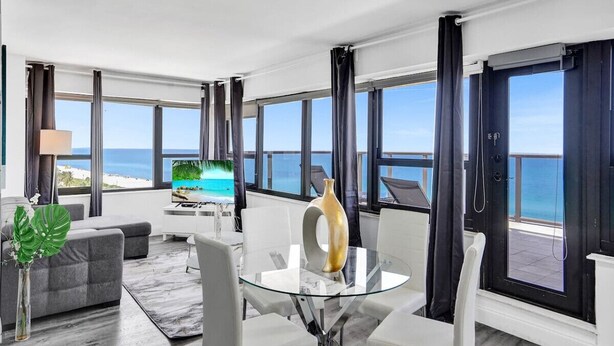 Een moderne hotelkamer met een ruim balkon, een glazen eettafel en een bank.