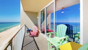A balcony with a view of the beach, a table, and green chairs. - Tidewater 1113 (Panama City Beach)