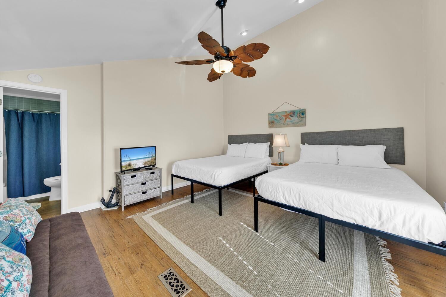 Ein Schlafzimmer mit zwei Betten, einem Deckenventilator, einem Fernseher und einem Badezimmer mit Duschvorhang.