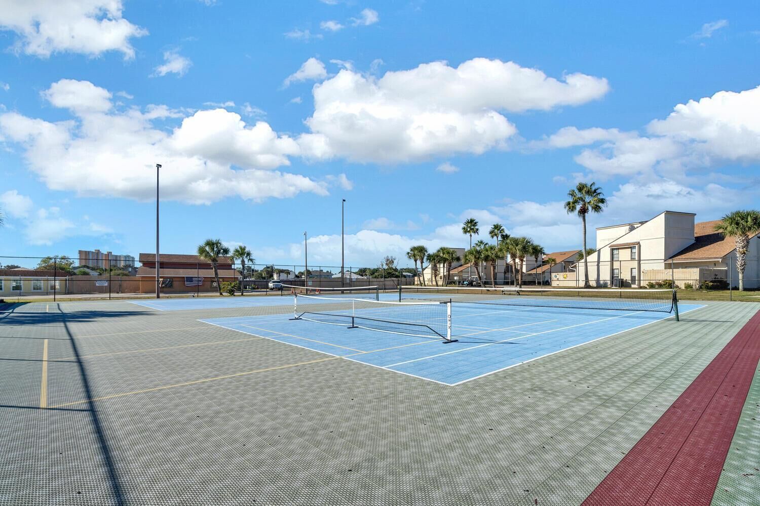 Un court de tennis en plein air, doté d’un filet, entouré d’une clôture et bordé de palmiers.