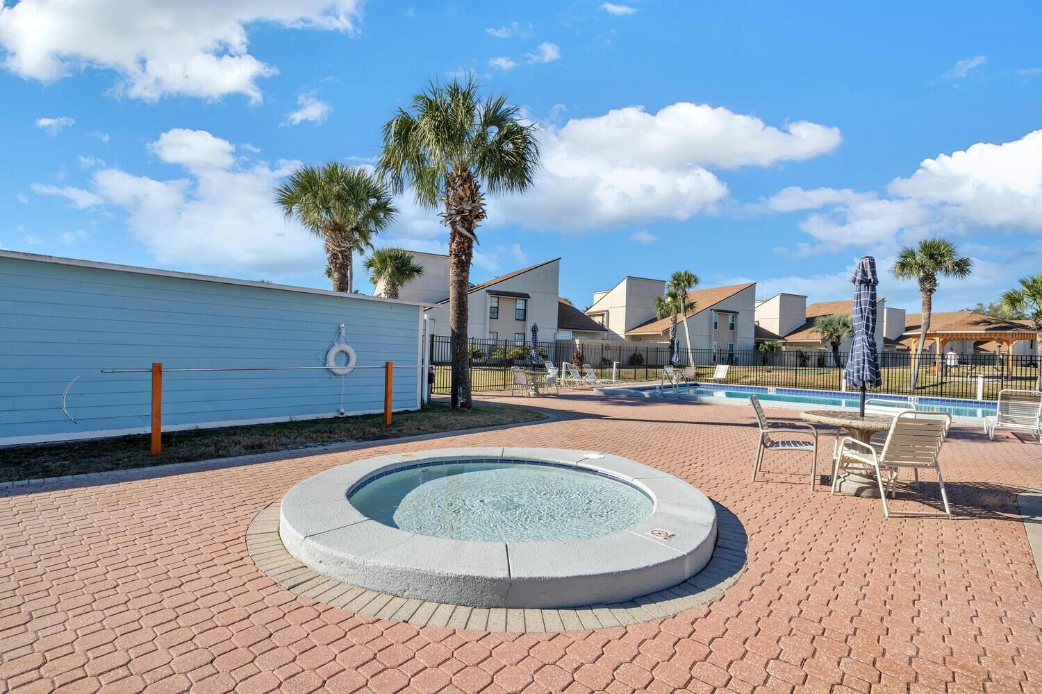 A pool area with a hot tub, lounge chairs, and palm trees.