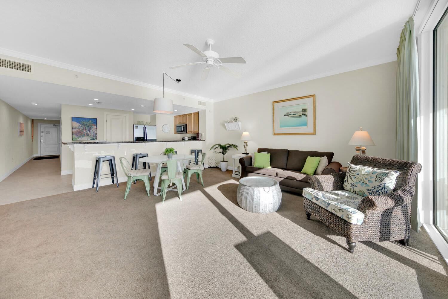 A spacious living room with a large window, a dining area, and a kitchen in the background.