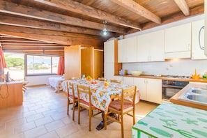 Techo con vigas de madera, una mesa de comedor con sillas, zona de cocina con armarios y vistas a través de una ventana.