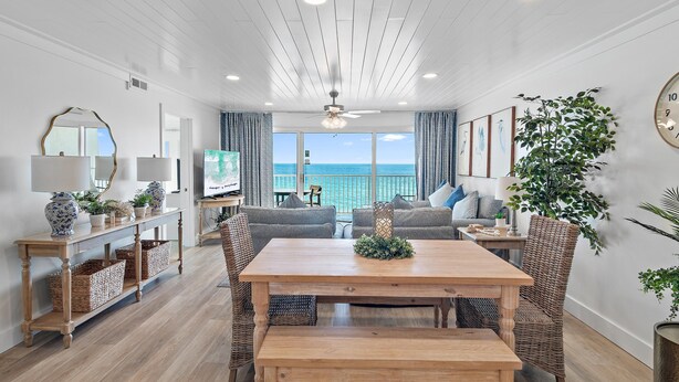 A spacious living area with a wooden dining table, wicker chairs, and a balcony with a view of the ocean. - Beach House 502d (Miramar Beach)