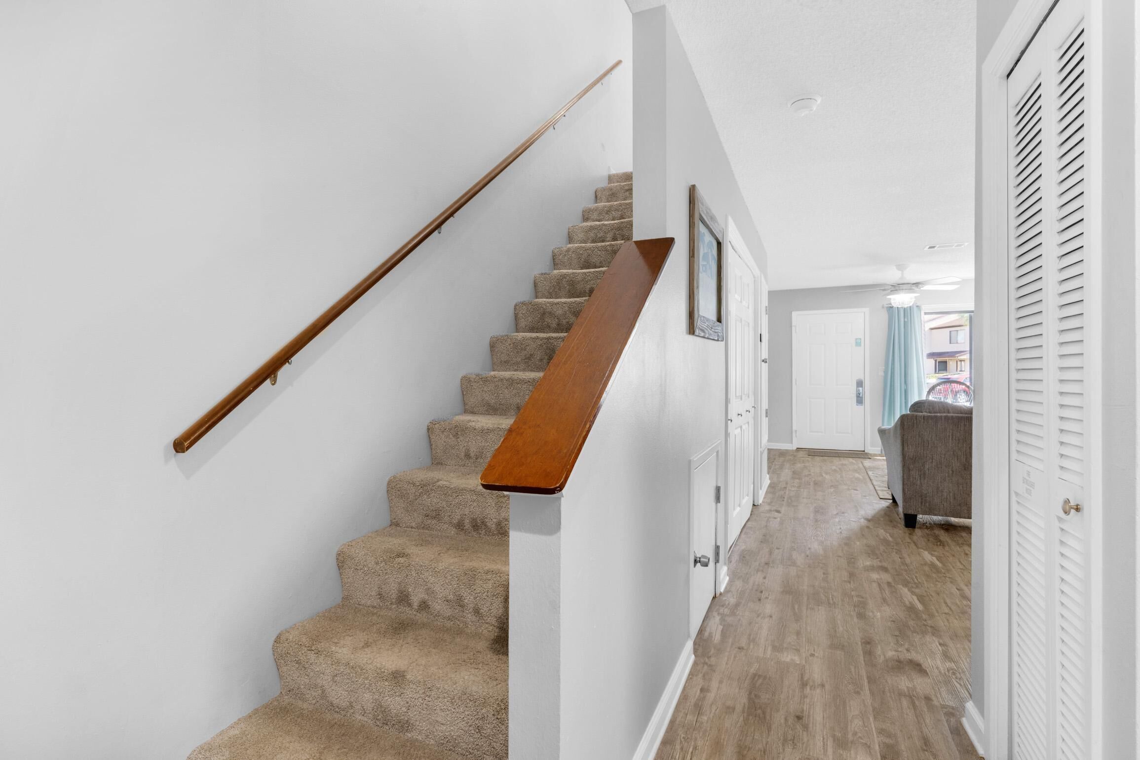 A staircase with a wooden handrail and carpeted steps leading to a door.