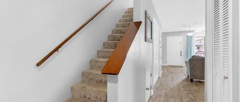 A staircase with a wooden handrail and carpeted steps leading to a door.