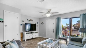 Ein Wohnzimmer mit einer Couch, einem Couchtisch, einem Fernseher und einem Deckenventilator.