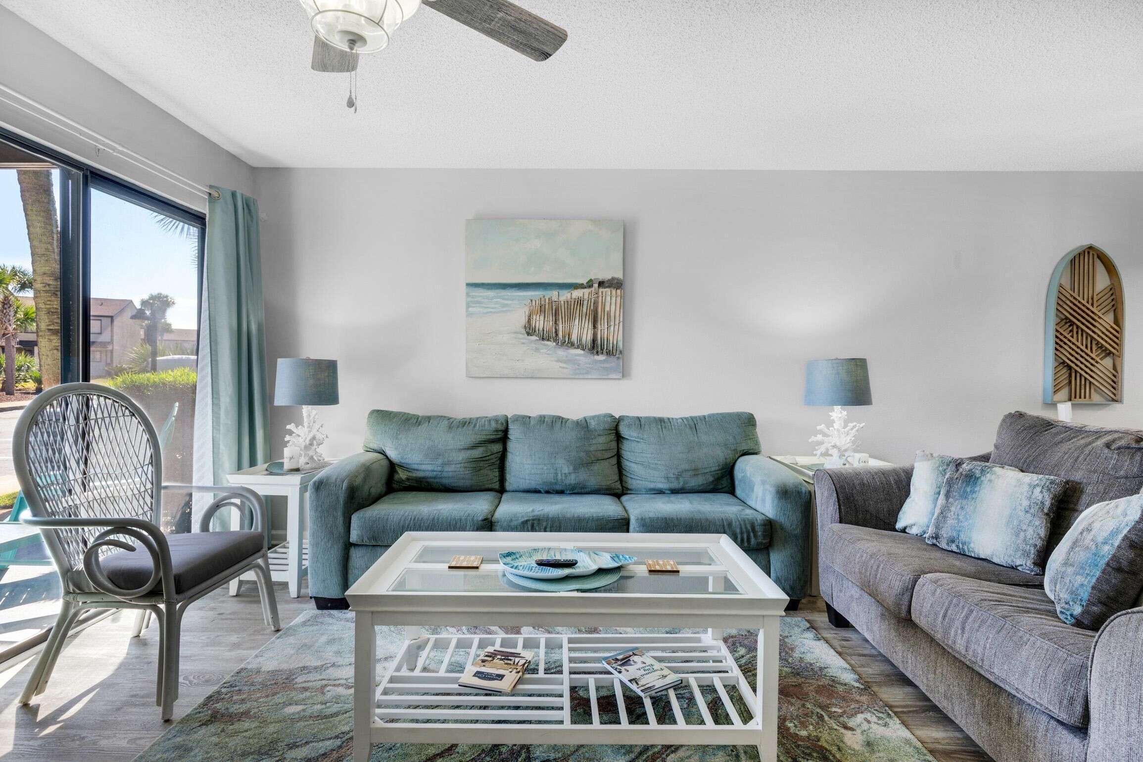 Un salon avec un canapé bleu, une table basse et un tableau représentant une scène de plage.